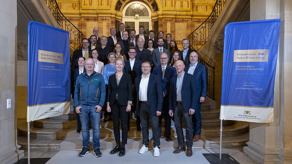 Mehrere Personen in schicker Kleidung stehen zusammen, rechts und Links stehen zwei dunkelblaue Plakate zum Klimabündnis Baden-Württemberg