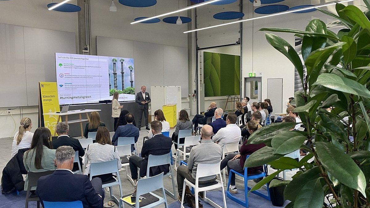 Vortrag eines Unternehmensvertreters bei Arnold Umformtechnik Dörzbach. Das Publikum hört einem Sprecher und einer Sprecherin zu.