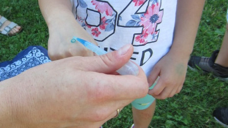 Ein Kindergartenmädchen erhält mit einer Pipette einen tropfen blaues Wasser auf die Hand.