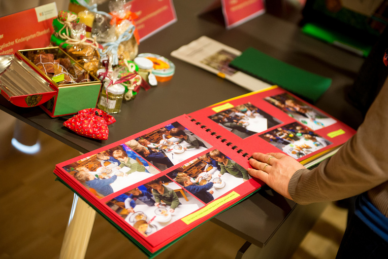 Ein Tisch, ein aufgeschlagenes Fotoalbum, Kinderfotos. Eine Hand liegt auf dem Buch. Geschenke liegen auf dem Tisch, Dose, Gläser, Säckchen