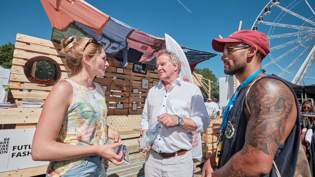 Minister Franz Untersteller unterhält sich mit einer Frau und einem Mann, im Hintergrund ist ein Riesenrad zu sehen
