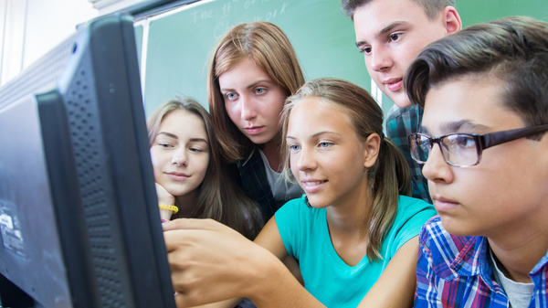 Drei Schülerinnen und zwei Schüler drängen sich um eine Computer und schauen gespannt auf den Bildschirm.