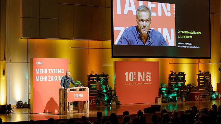 Auf der Bühne des Jubiläumskongresses "10 Jahre Nachhaltigkeitsstrategie Baden-Württemberg" spricht Hannes Jaenicke zum Publikum.