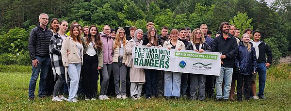 Beteiligte Menschen am Projekt des World Ranger Days 2025 stehen zusammen und halten ein Banner.