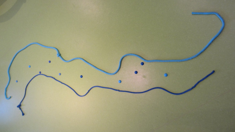 Zwei Fäden liegen wellenförmig und parallel auf dem Boden und stellen einen Flusslauf dar.
