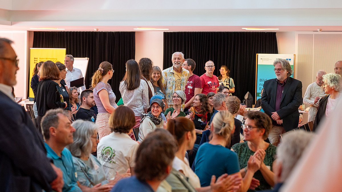 Teilnehmende beim BNE-Festival im Paul-Lechler Saal; sie klatschen, lachen und schauen im Saal herum.