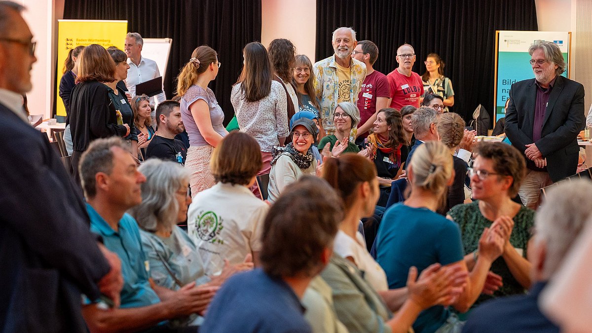 Teilnehmende beim BNE-Festival im Paul-Lechler Saal; sie klatschen, lachen und schauen im Saal herum.