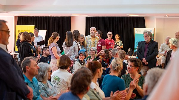 Teilnehmende beim BNE-Festival im Paul-Lechler Saal; sie klatschen, lachen und schauen im Saal herum.