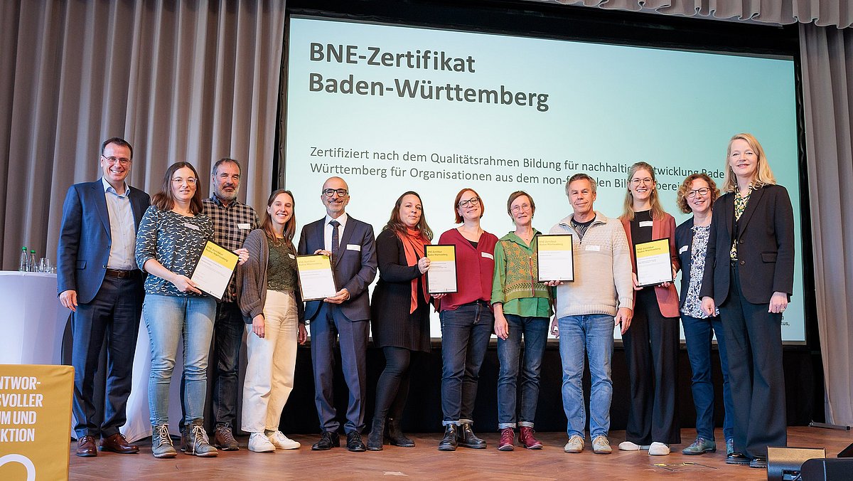 Die Empfängerinnen und Empfänger der BNE-Zertifikate stehen gemeinsam mit der Umweltministerin Thekla Walker und Staatssekretär im Kultusministerium Volker Schebesta stehen gemeinsam zum Gruppenbild auf der Bühne des Netzwerkforums BNE-BW 2030.
