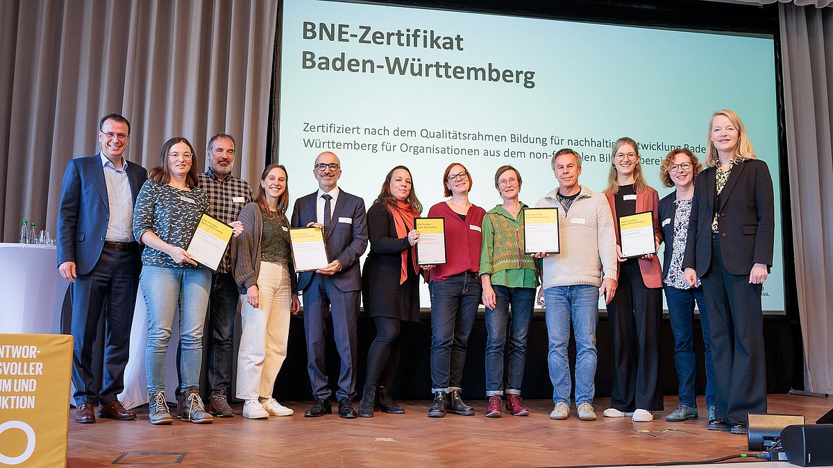 Die Empfängerinnen und Empfänger der BNE-Zertifikate stehen gemeinsam mit der Umweltministerin Thekla Walker und Staatssekretär im Kultusministerium Volker Schebesta stehen gemeinsam zum Gruppenbild auf der Bühne des Netzwerkforums BNE-BW 2030.