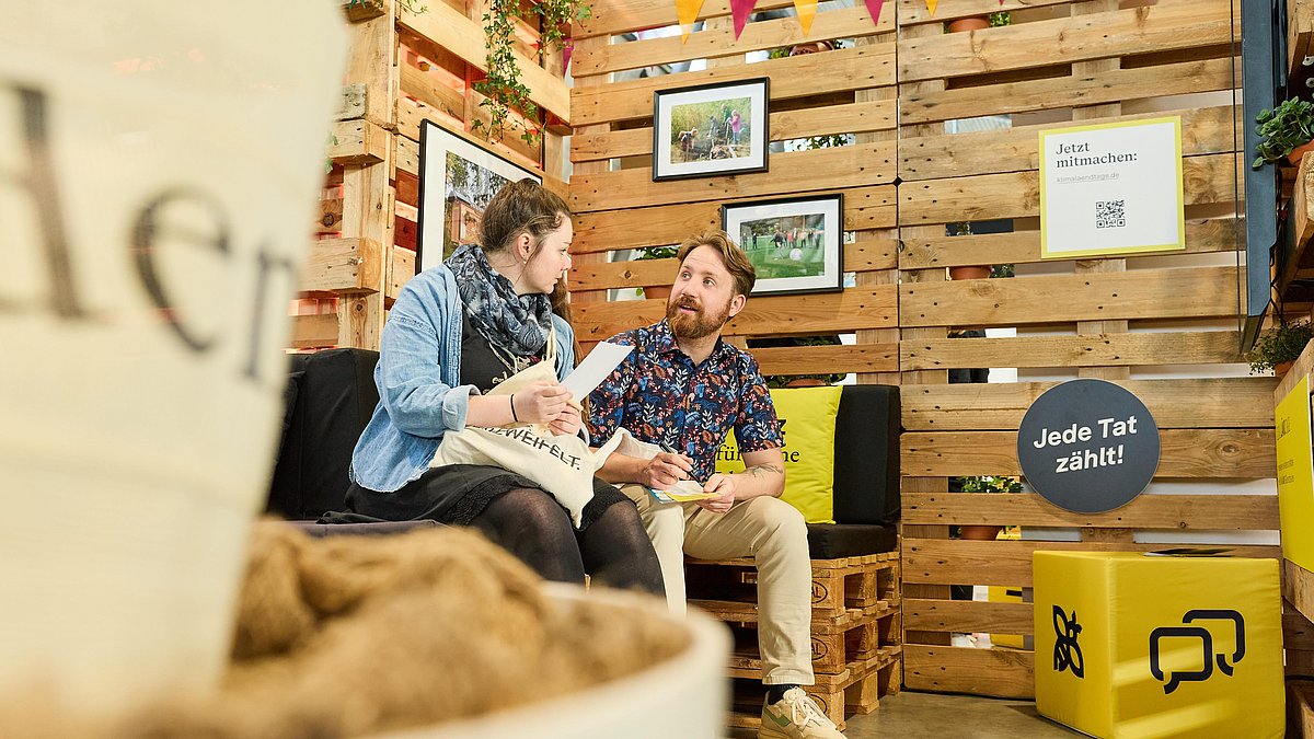 Ein Mann und eine Frau unterhalten sich sitzend am Stand der Nachhaltigkeitsstrategie.