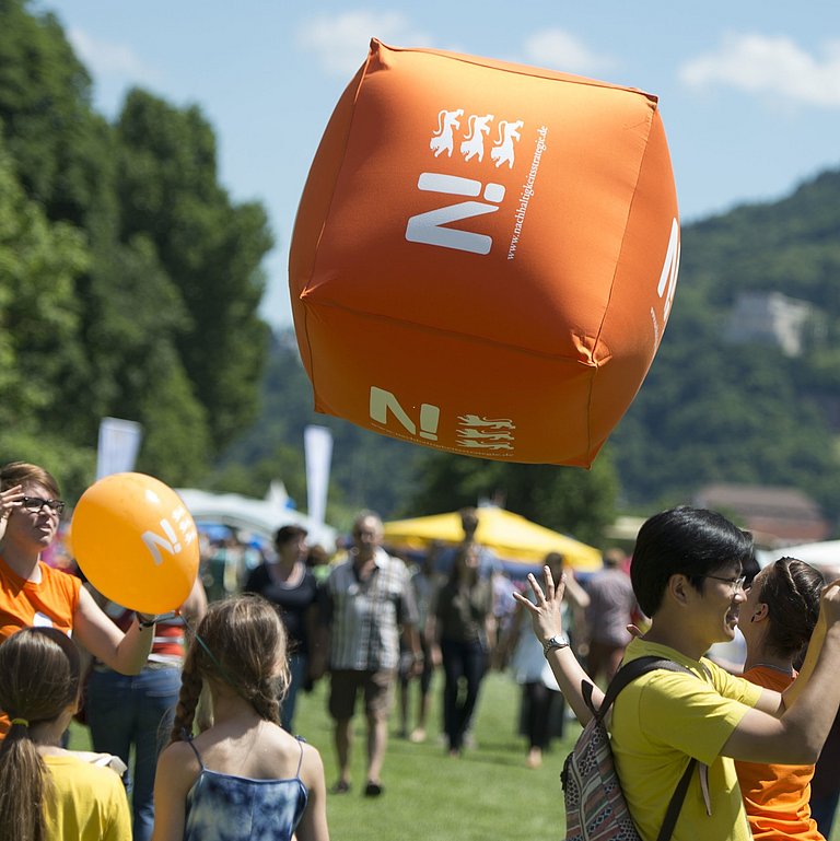 Bei einer Veranstaltung im Freien mit vielen Leuten aus jeder Altersgruppe wird ein großer Nachhaltigkeitswürfel in die Luft geworfen.