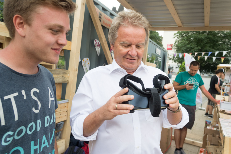 Herr Minister Franz Untersteller hält an einem Stand des Übermorgen Markts eine VR Brille in der Hand 