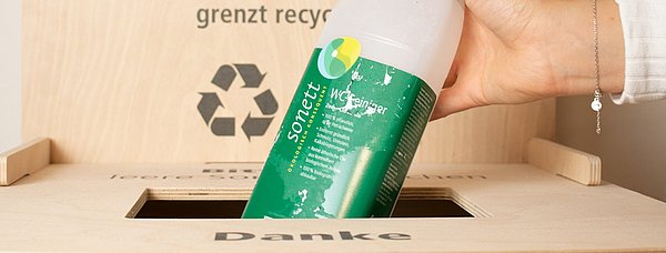 Die Sonett Rücknahmebox aus Holz und eine Hand, die einen leeren Sonett WC-Reiniger hineinwirft.