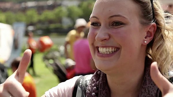 Gelebte Nachhaltigkeit Eine fröhlich strahlende Frau zeigt bei einer Nachhaltigkeitsveranstaltung beide Daumen in die Höhe.