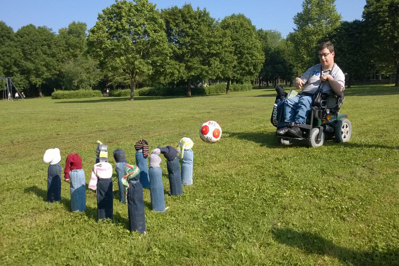 ein Junge im Rollstuhl spielt auf einer Wiese Bowling