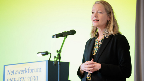 Das Farbfoto zeigt eine Nahaufnahme der Umweltministerin Thekla Walker MdL. Sie spricht auf einer Bühne an einem Rednerpult mit Mikrofon. Auf dem Pult steht „Netzwerkforum BNE-BW 2030”.