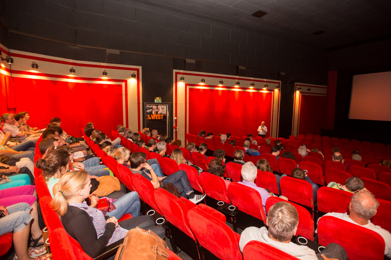 Ein Kinosaal mit roten Sitzen. Die Sitzreihen mit Menschen besetzt.