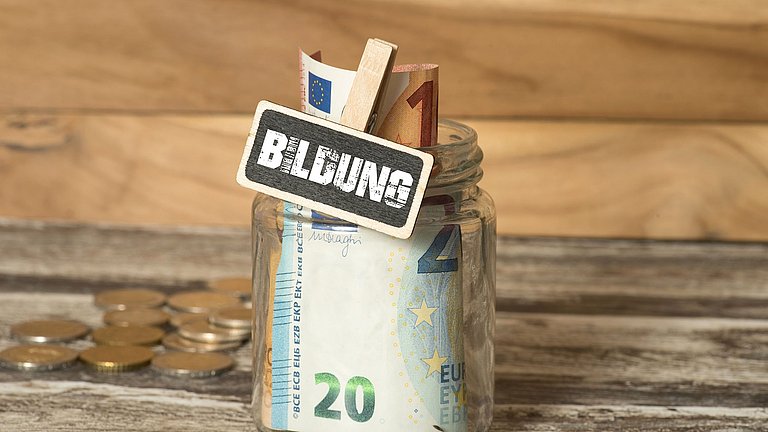 Geldscheine in einem Weckglas und Münzen im Hintergrund.