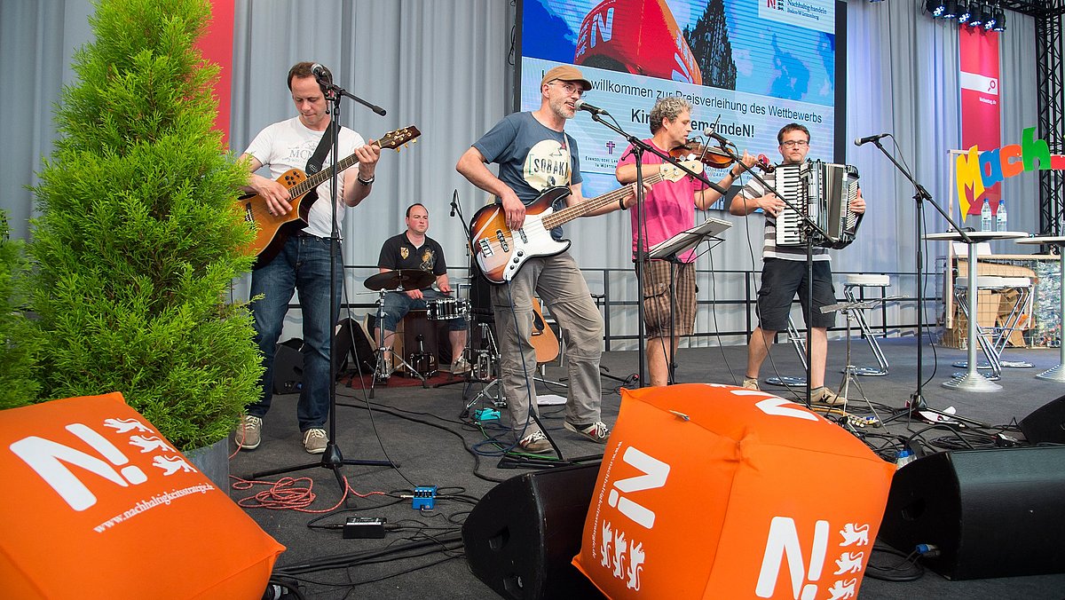Fünf Musiker mit Gitarren, Geige, Akkordeon und Schlagzeug sorgen beim Deutschen Ev. Kirchentag in Stuttgart auf der Bühne der Nachhaltigkeitsstrategie  für Unterhaltung.
