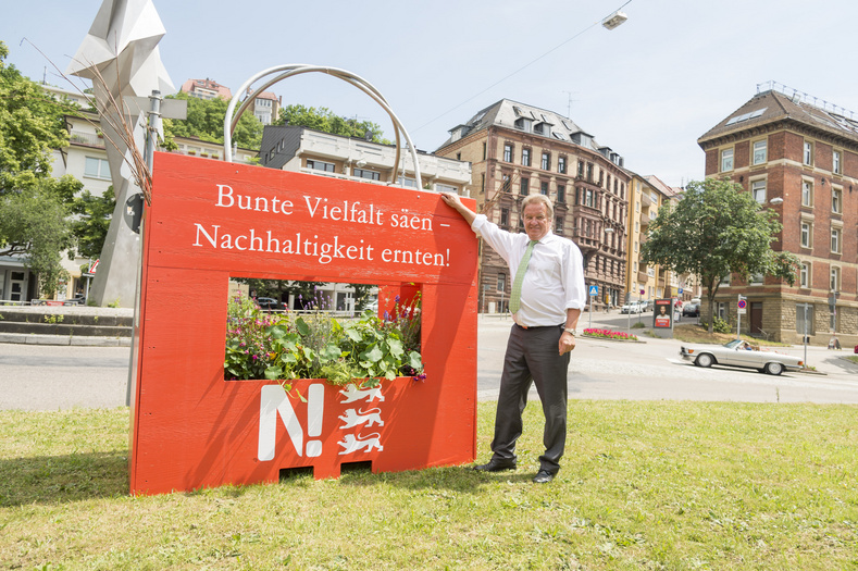 Franz Untersteller posiert mit übergroßer Pflanztasche vor dem Umweltministerium 