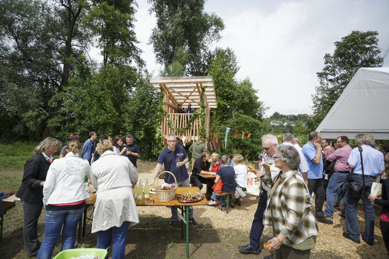 Ca. 25 Personen im Freien. Das Baumhaus im Hintergrund. Ein Biertisch mit Obst und Limonade.