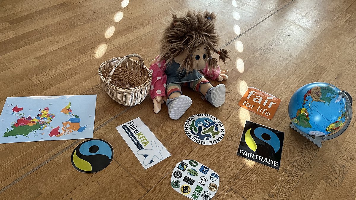 Ilse-Lotte, unsere Handpuppe führt das Thema im Stuhlkreis ein. Sie bringt einen Korb mit fairen Logos mit.