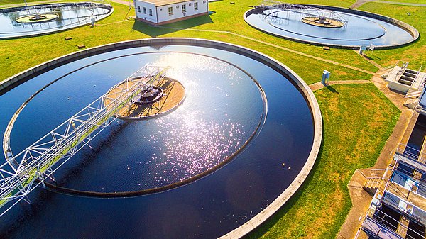 Zu sehen sind vier von oben fotograftierte runde Becken einer Kläranalge, im Hintergrund Bäume.