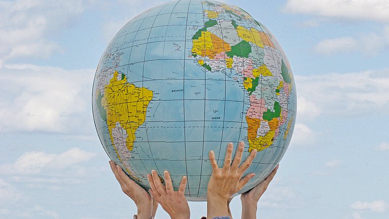 Mehrere Hände halten eine Weltkugel in den Himmel hoch.