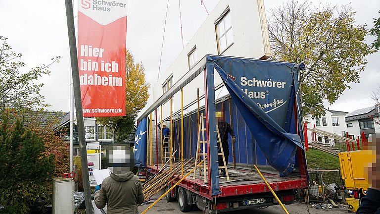 Eine Fertighauswand wurde abgebaut und wird auf einen großen LKW-Anhänger verladen.