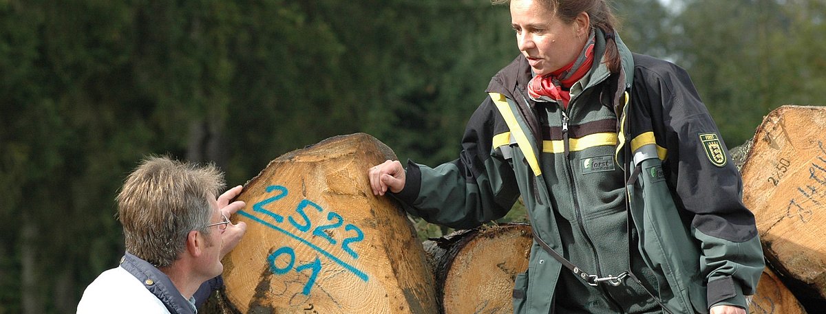 Ein Holzeinkäufer und eine Mitarbeiterin von Forst BW begutachten ein Holzlager im Wald.