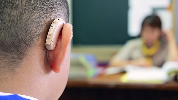 Dargestellt ist ein Schüler mit Hörgerät im Klassenzimmer.