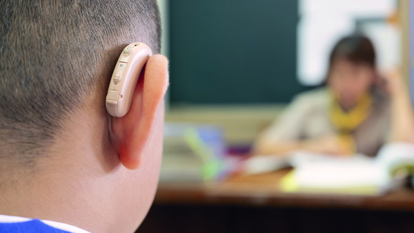 Dargestellt ist ein Schüler mit Hörgerät im Klassenzimmer.