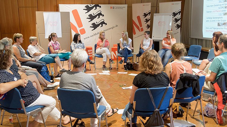 Erzieherinnen und Erzieher sitzen in einem Stuhlkreis.