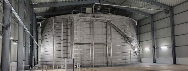 Großbehälter in Flachdachbauweise mit Treppenanlage in einer Stahlhalle.