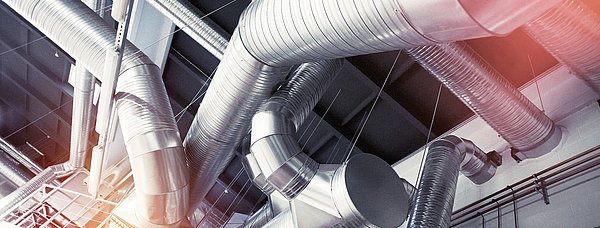 Eine großes Lüftungsrohrgeflecht durchzieht den Deckenbereich einer Produktionshalle.