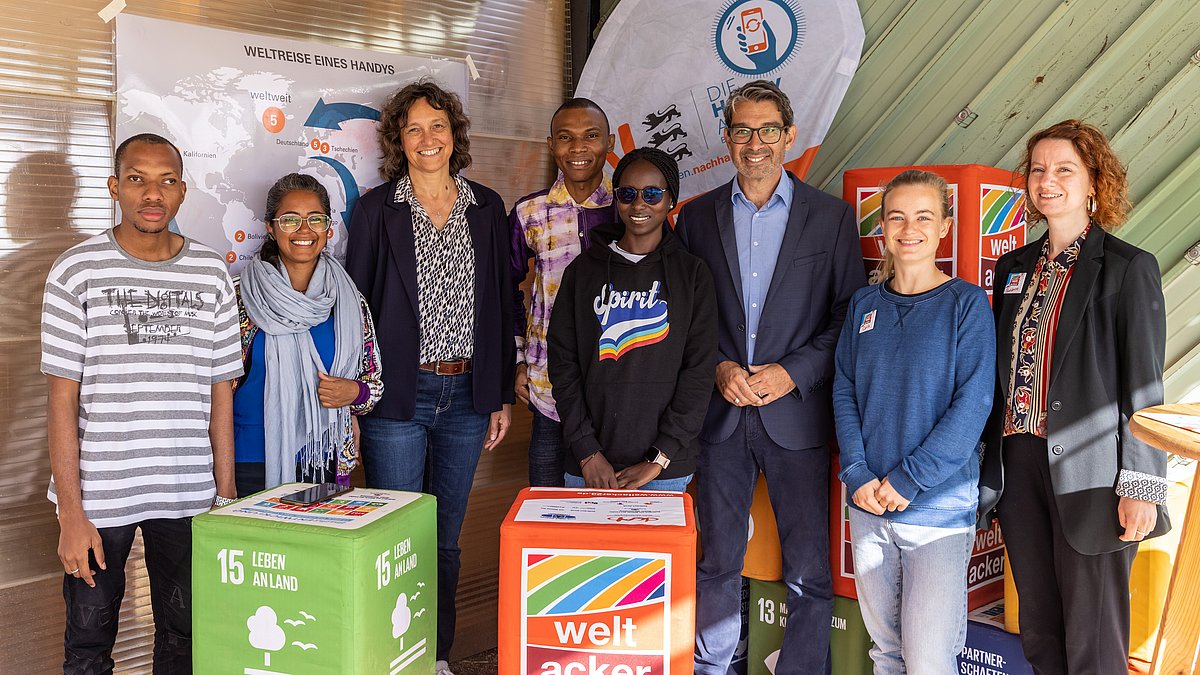 Mehrere Personen stehen nebeneinander innerhalb des Standes der Handy-Aktion BW. Hinter Ihnen ist eine dazu passende Flagge aufgestellt und rings herum große bunte Würfel mit Aufschrift.