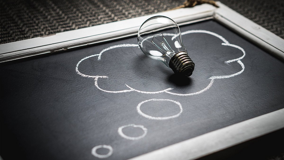 Auf  einer alten Tafel ist eine Gedankewolke aufgemalt. Auf dieser liegt eine Glühbirne.