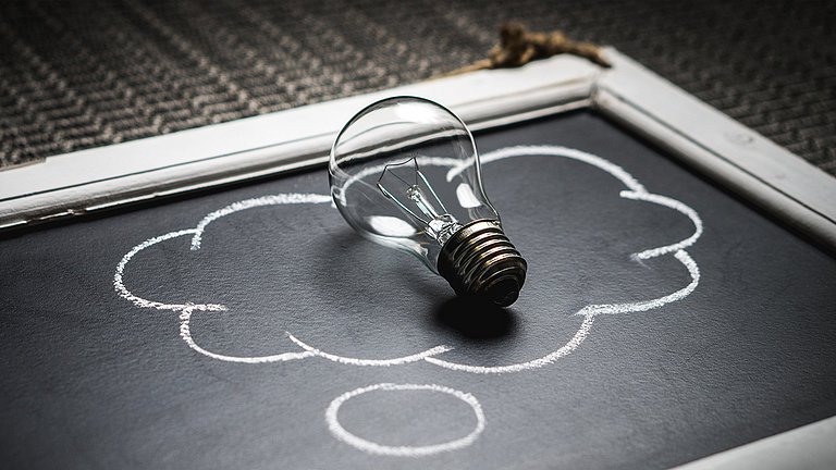 Auf  einer alten Tafel ist eine Gedankewolke aufgemalt. Auf dieser liegt eine Glühbirne.