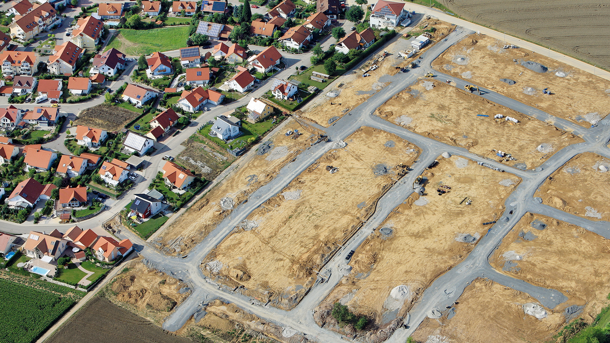 Flächenmanagement Ein Luftbild von einem Neubaugebiet, das gerade erschlossen wird. Straßen werden neu angelegt und durchziehen das Gelände. Links des Neubaugebiets schließt die bestehende Bebauung an.