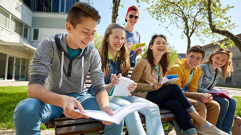 Sechs Schüler im Freien auf einer Bank sitzend und lachend.