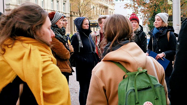 Eine Gruppe von über 8 Frauen und Männer erhalten im Rahmen einer Stadtführung Informationen über Stuttgart.