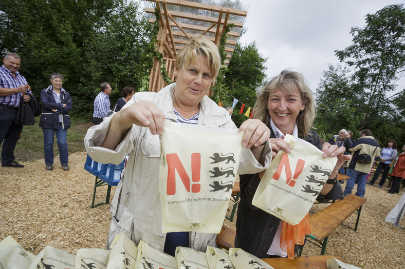 Nachhaltigkeitstage 2014 Einweihungsfest am Baumhaus. Zwei Frauen halten N-Strategie-Stoffbeutel hoch und blicken in die Kamera.