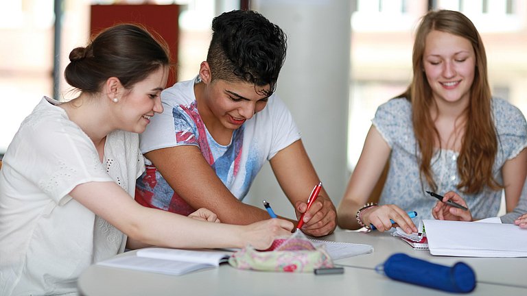 Zwei Berufsschülerinnen und ein Berufsschüler sitzen am Tisch und lernen gemeinsam.