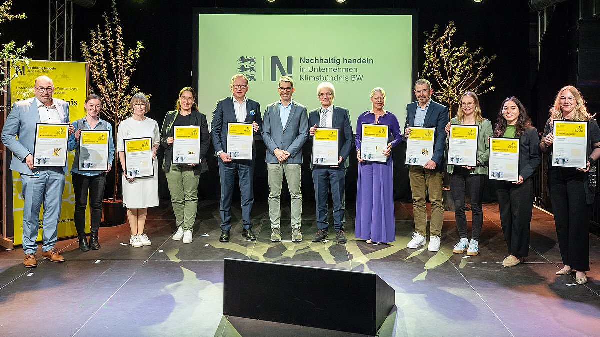 Die Vertreter und Vertreterinnen der neuen Klimabündnis BW Unternehmen stehen mit Staatssekretät Andre Baumann zu einem Gruppenbild zusammen mit ihren Urkunden in den Händen.