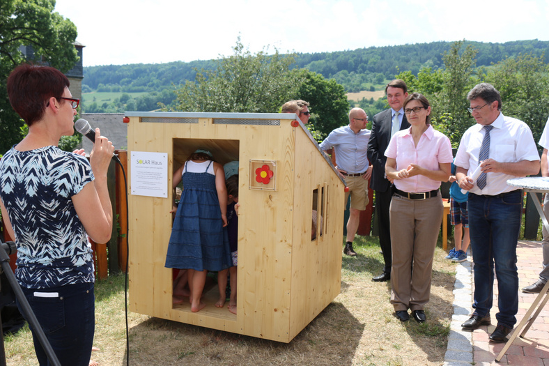 Eine Frau präsentiert ein von Schreinermeister Pommert gebautes Solarhaus mit PV-Anlage für den Kindergarten Schäfersheim