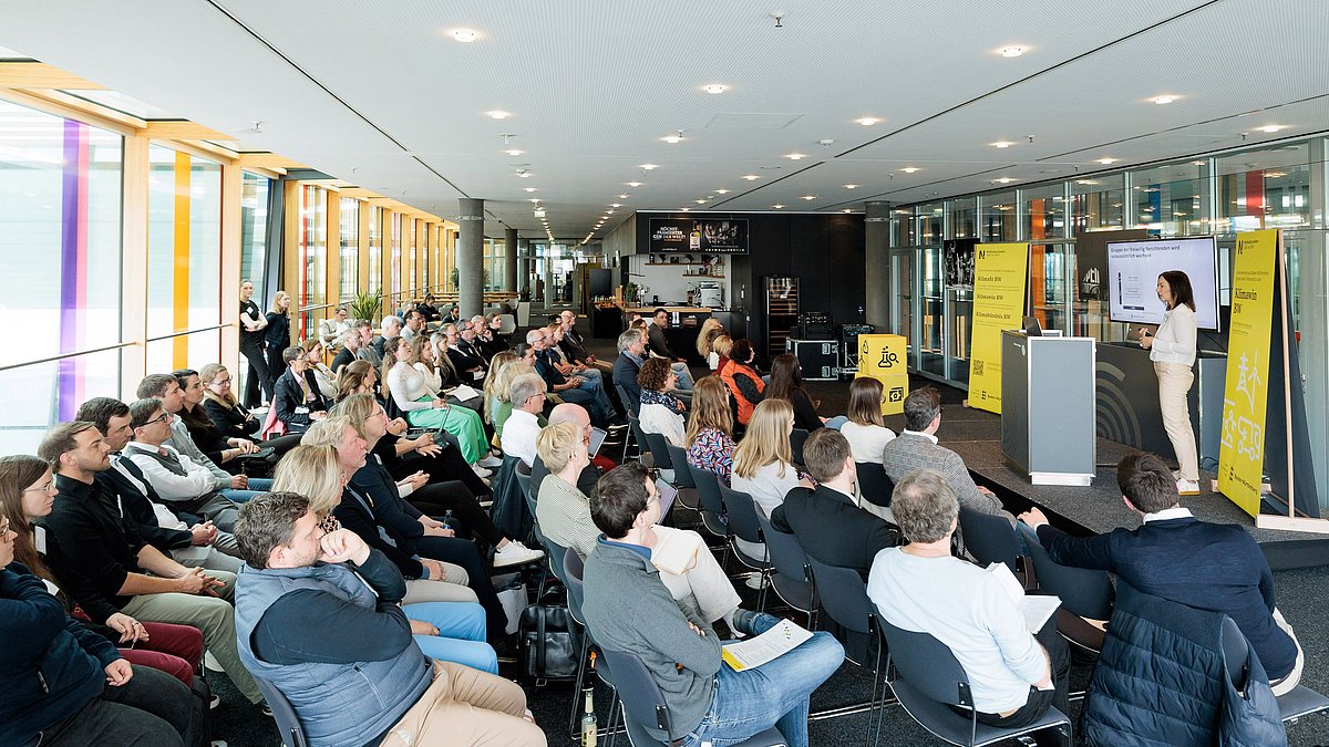 Frau steht auf der Bühne vor einem großen Publikum und erklärt etwas am Bildschirm.
