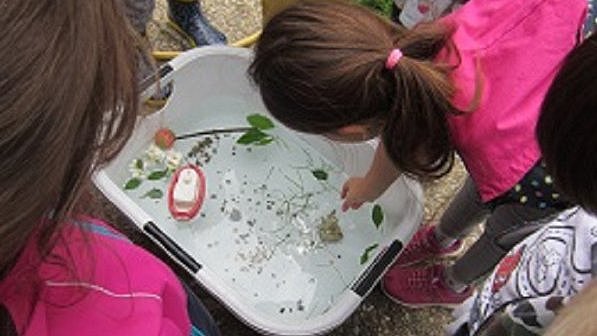 Kinder stehen um eine kleine Wanne herum, die mit Wasser gefüllt ist und in der ein Schiffchen schwimmt.