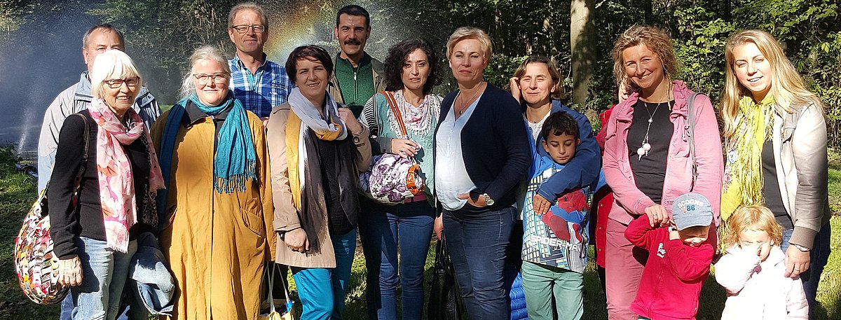 Eine Gruppe von 15 Personen, darunter drei Kinder,  stehen für ein Gruppenbild auf der Wiese. Im Hintergrund sind Bäume.