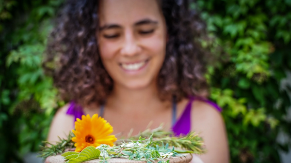 Eine Frau häkt lächelnd Blumen in die Kamera.